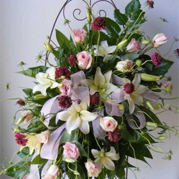 Tall floral spray with white lilies, pink roses, and lavender ribbon on a metal stand