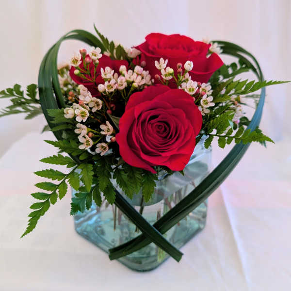Red roses with small white blossoms in a glass vase