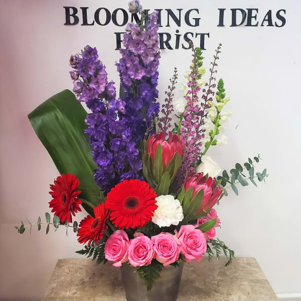 Tall mixed flower arrangement in a metal bucket with pink roses and red gerbera daisies