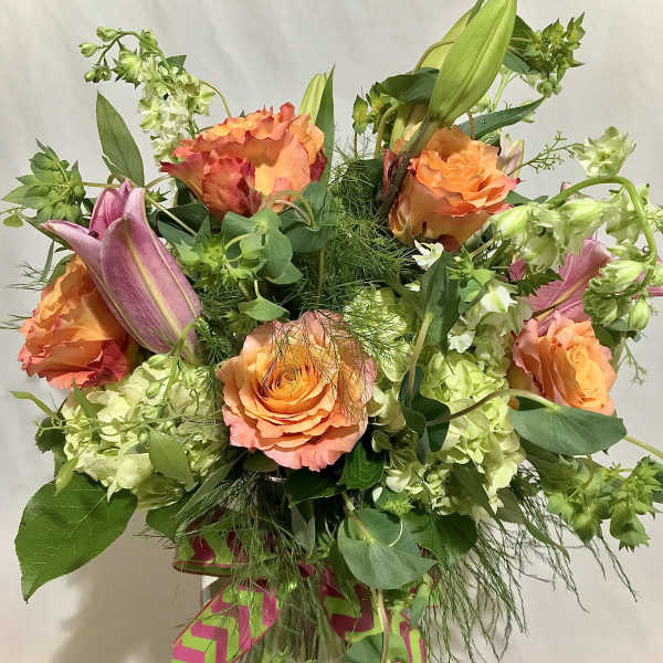 Tall arrangement of orange roses, pink lilies, and green hydrangeas in a clear glass vase