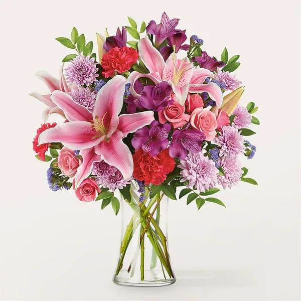 Pink lilies and mixed flowers in a clear glass vase