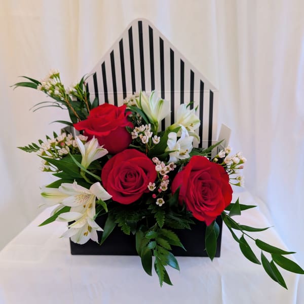 Red roses and white lilies arranged in a black box with a striped back panel.