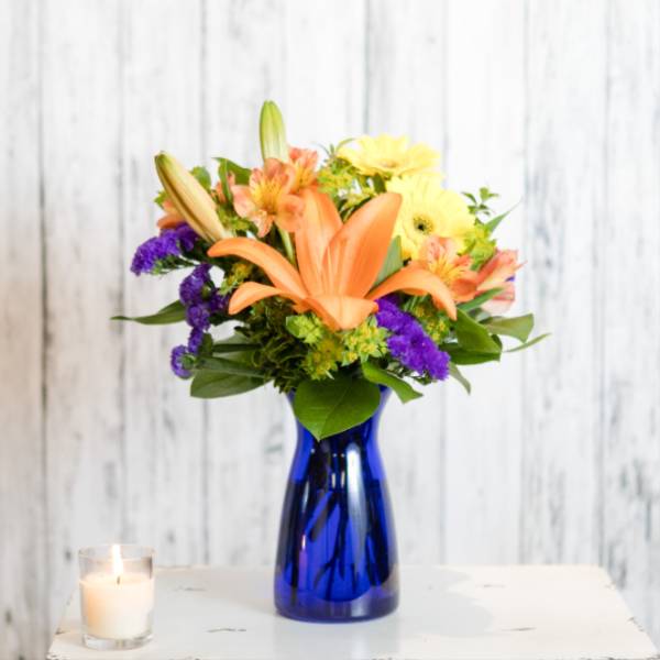 Bouquet of orange lilies, yellow daisies, and purple flowers in a blue vase