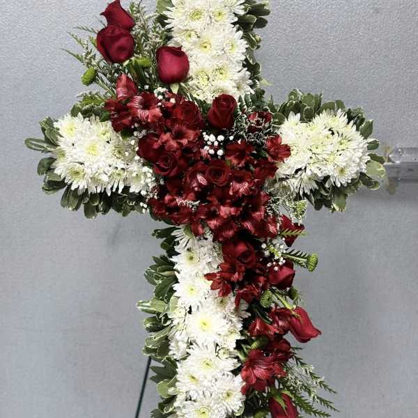 Standing floral cross of white mums and red roses displayed on a metal easel.
