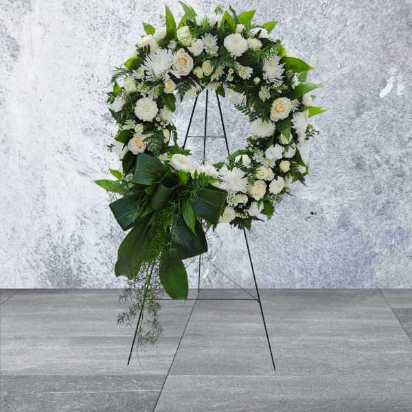 White floral wreath on a black stand with green foliage