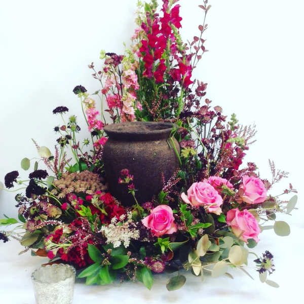Pink roses and mixed flowers arranged around a dark urn centerpiece