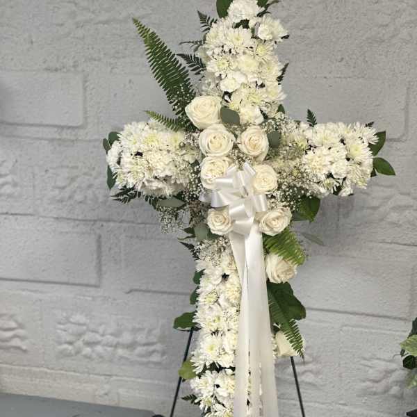 White floral cross arrangement with roses and chrysanthemums on an easel