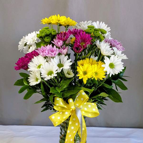 Mixed daisy bouquet in a glass vase with a yellow polka-dot ribbon