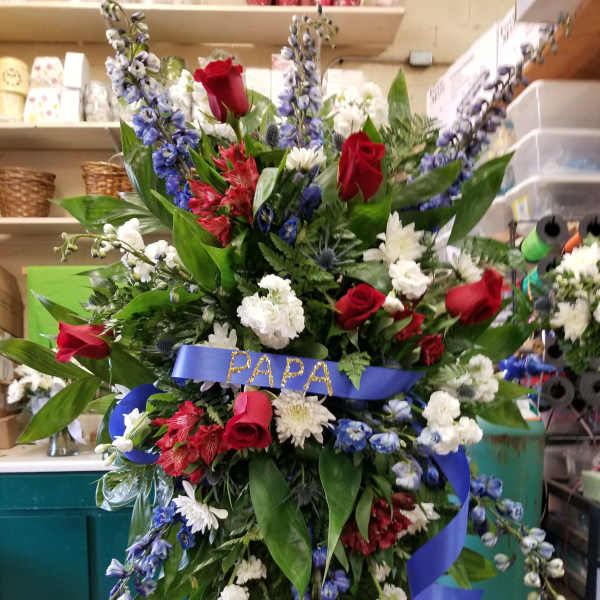 Large standing floral spray with red roses, white blooms, and blue flowers on a ribboned easel