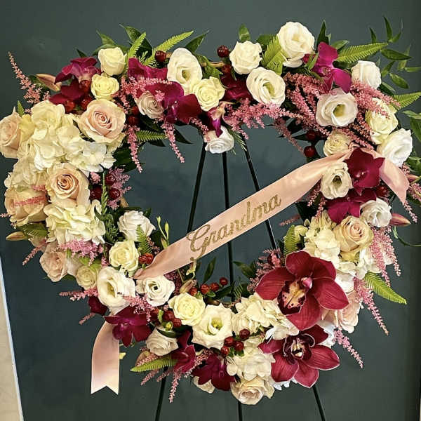 Heart-shaped floral wreath with roses, orchids, and a pink ribbon