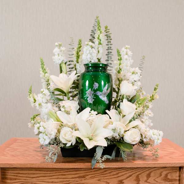 White lilies and roses arranged around a green urn centerpiece