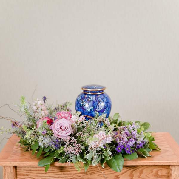 Low floral arrangement with pink and purple roses around a blue urn