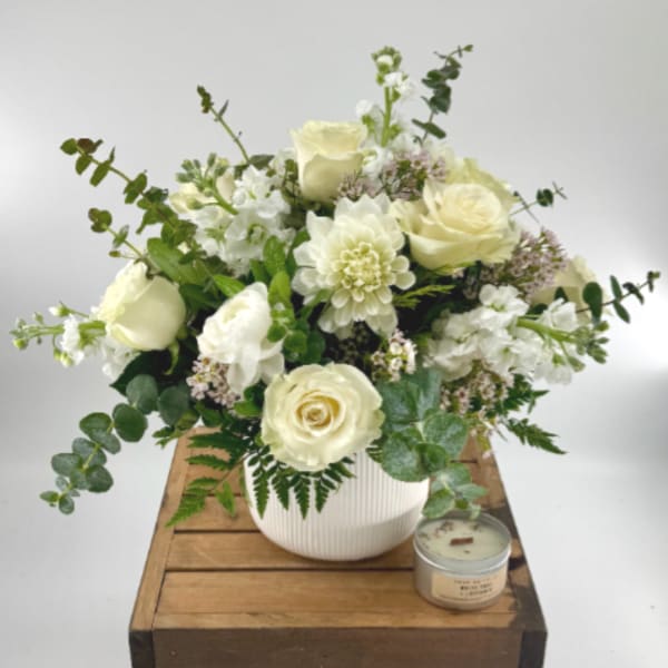 Cream rose and white flower arrangement in a white vase with a candle