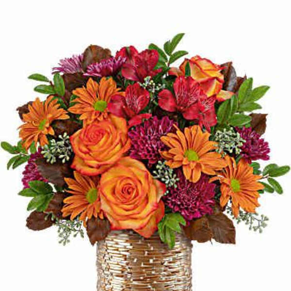 Orange and red mixed flower arrangement in a woven basket vase