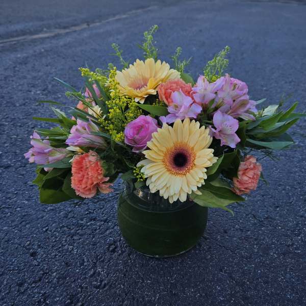 Mixed bouquet in a glass vase with yellow gerberas, pink roses, and coral carnations