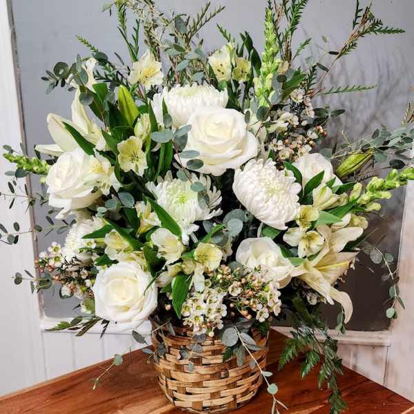 White floral arrangement in a woven basket with roses and lilies
