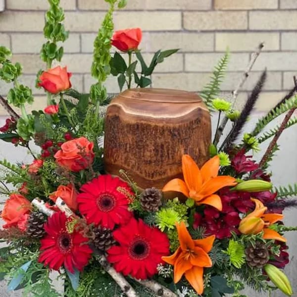Bright mixed floral arrangement with roses, gerbera daisies, and lilies around a wooden urn