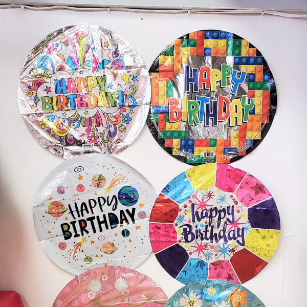 Six round birthday balloons with colorful printed designs on a wall