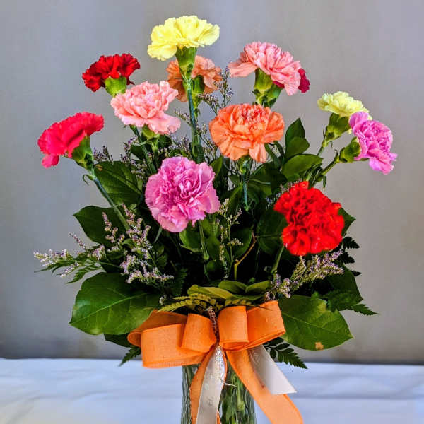 Colorful carnations in a glass vase with an orange ribbon