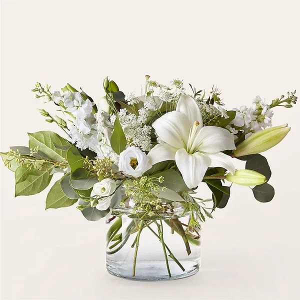 White lilies and mixed white flowers in a clear glass vase