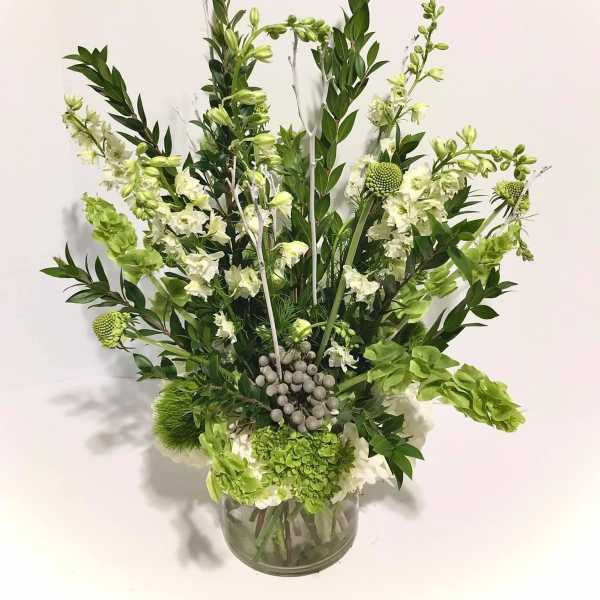 Tall green and white floral arrangement with hydrangeas and bells of Ireland in a clear glass vase.