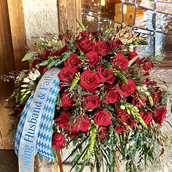 Tall standing spray of red roses with cascading greenery and a memorial ribbon on an easel.