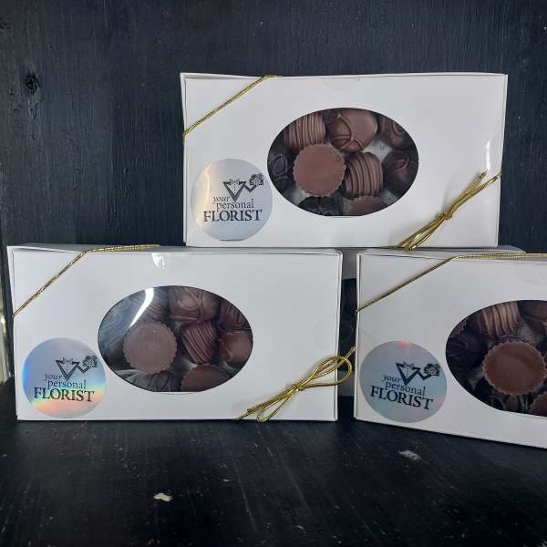 Three white window boxes of assorted chocolates tied with gold cord on a dark surface