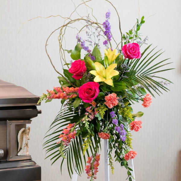 Tall funeral spray with pink roses, yellow lilies, and hanging carnations