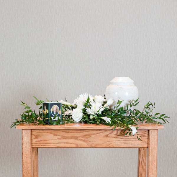 White floral funeral arrangement with an urn and memorial candle