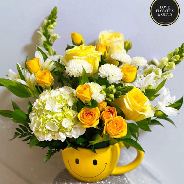 Cheerful yellow and white flower arrangement in a yellow smiley-face mug