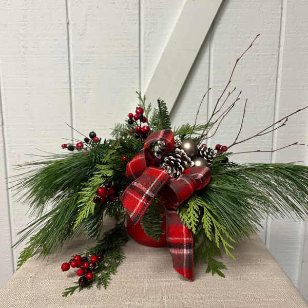 Holiday arrangement with pine, berries, pinecones, and a red plaid ribbon in a red container
