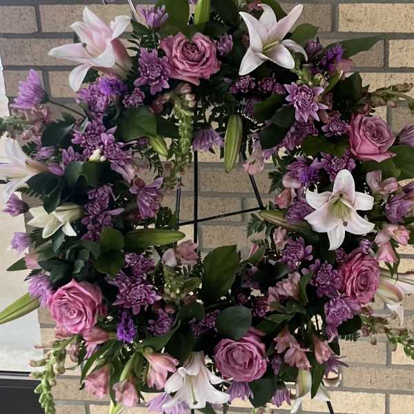 Round floral wreath with pink roses, white lilies, and purple blooms