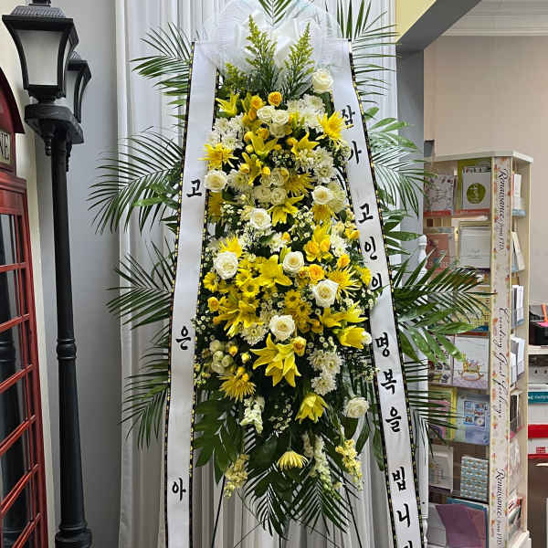 Tall standing floral wreath with yellow and white flowers on a ribboned easel