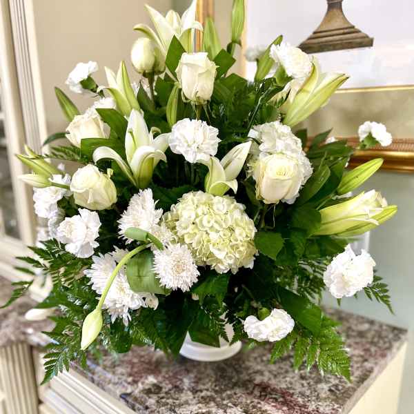 White floral arrangement with lilies, roses, hydrangea, and carnations in a vase