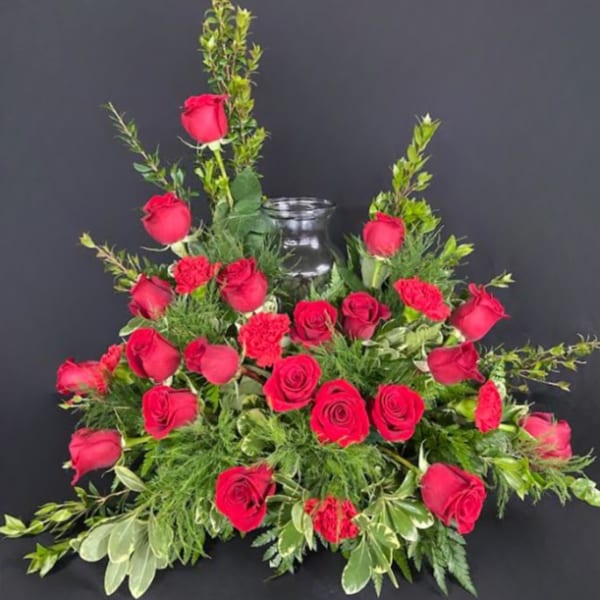 Red roses arranged around a clear glass vase with greenery