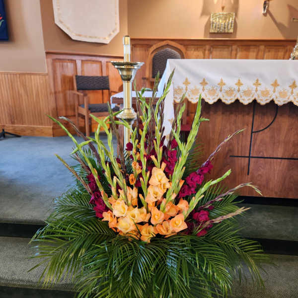 Tall floral altar arrangement with peach and burgundy flowers and palm fronds