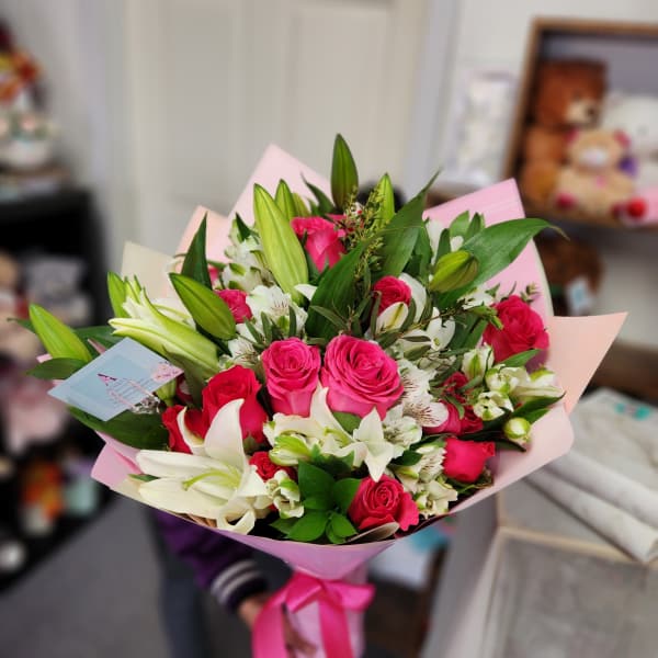 Bouquet of pink roses and white lilies wrapped in pink paper
