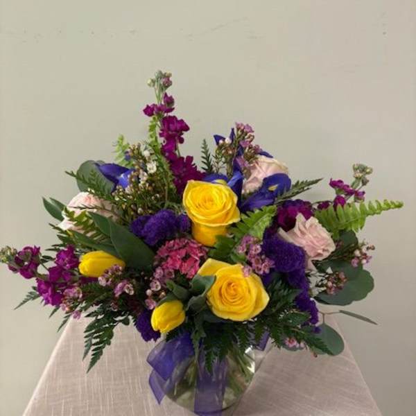 Bouquet of yellow and purple flowers in a glass vase with a ribbon