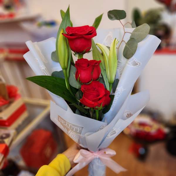 Bouquet of red roses and unopened lilies wrapped in white paper