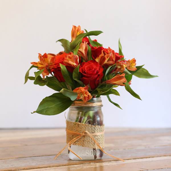 Red roses and orange alstroemeria in a mason jar vase