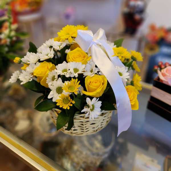 Yellow roses and white daisies in a wicker basket with a white ribbon