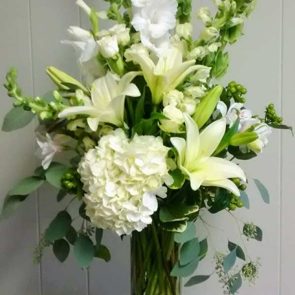 White lilies and hydrangea in a clear glass vase with tall green spikes