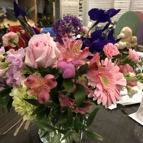 Mixed bouquet with pink roses, gerbera daisies, and purple blooms in a glass vase