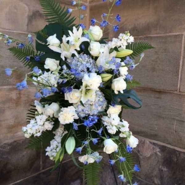 Tall standing spray of white lilies and roses with blue flowers on an easel