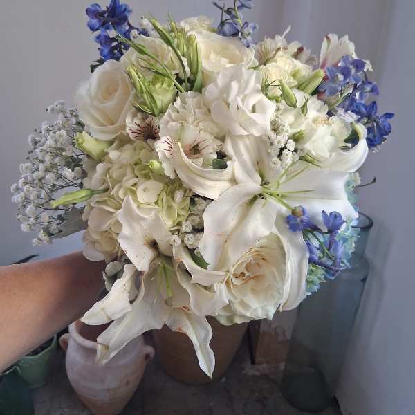 White bouquet with blue flowers and lilies held in hand