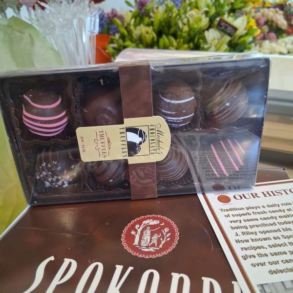 Box of assorted chocolate truffles on a counter with flower bouquets behind it