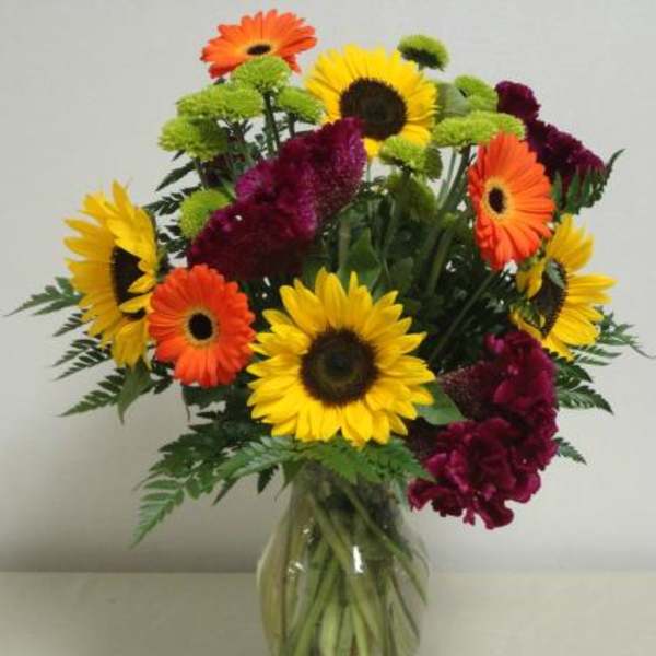 Bouquet of sunflowers, gerbera daisies, and burgundy flowers in a glass vase