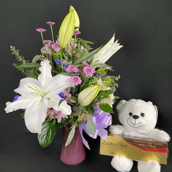 Bouquet of white lilies and pink flowers in a vase with a teddy bear and chocolates