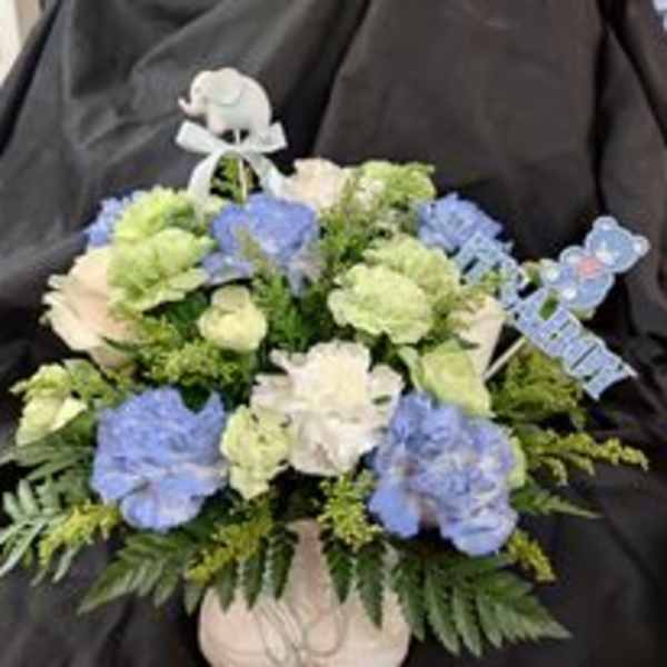 Blue and white floral arrangement in a white vase with ribbon picks