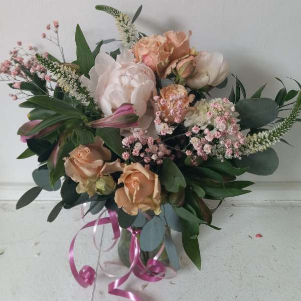 Peach and blush bouquet in a glass vase with pink ribbon